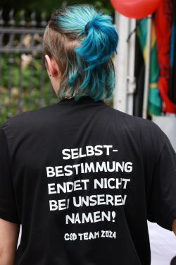 Foto einer Person, die das CSD Team 2024 Shirt trägt, auf dem das Motto "Selbstbestimmung endet nicht bei unseren Namen!" abgebildet ist